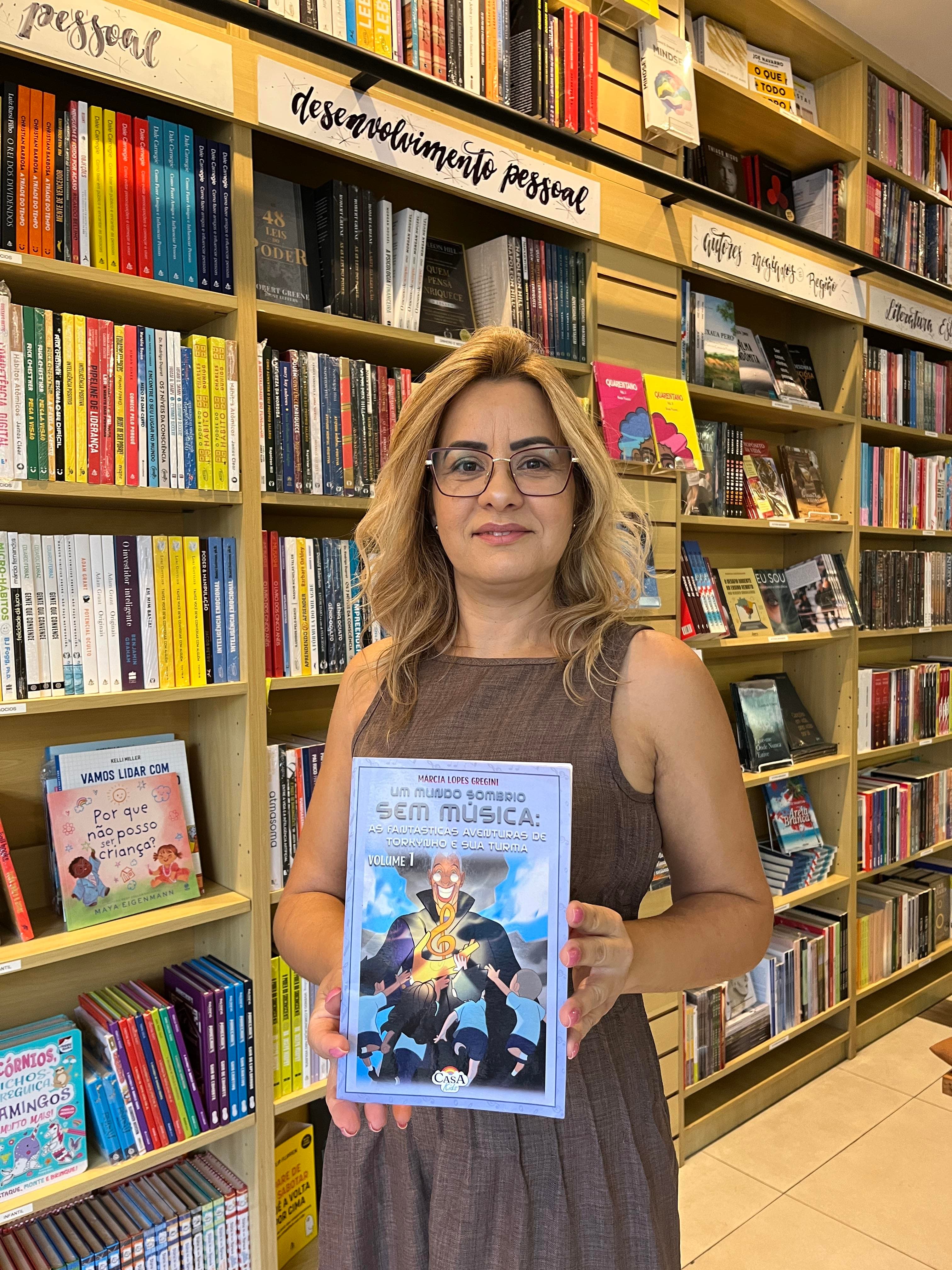 Márcia Lopes Gregini, autora, segurando o livro Um Mundo Sombrio sem Música em uma livraria